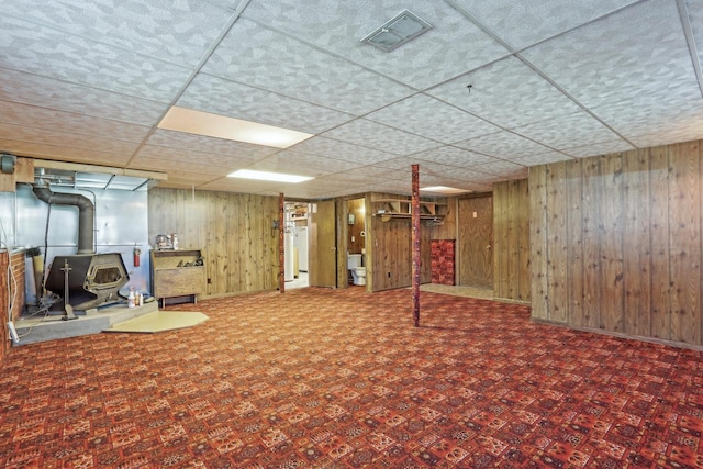 finished basement featuring a paneled ceiling, visible vents, water heater, and wood walls