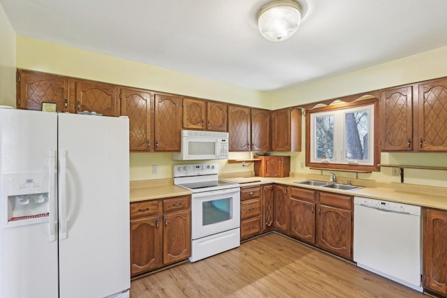 kitchen with white appliances, brown cabinetry, light wood-style floors, light countertops, and a sink