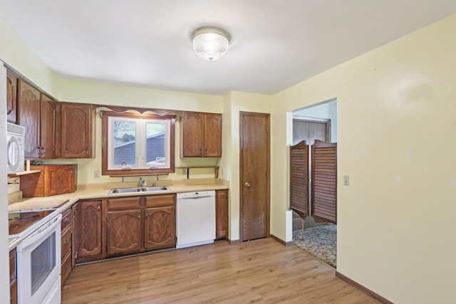 kitchen featuring a sink, white appliances, baseboards, light wood-style flooring, and light countertops