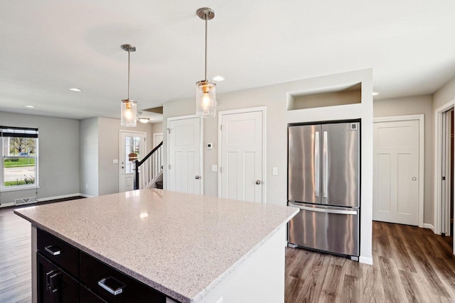 1059 Okeeffe Ave, Sun Prairie, WI 53590 - kitchen with freestanding refrigerator, light wood finished floors, hanging light fixtures, dark cabinetry, and light stone countertops