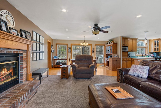 living room featuring recessed lighting, a fireplace, light carpet, and ceiling fan with notable chandelier