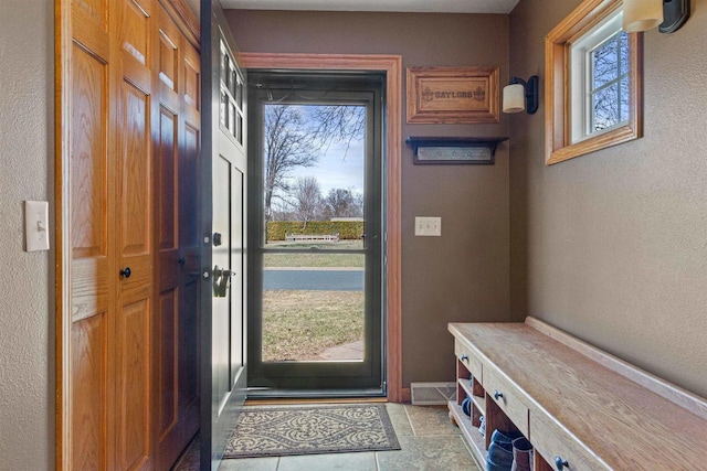 doorway featuring stone finish flooring, baseboards, a textured wall, and plenty of natural light