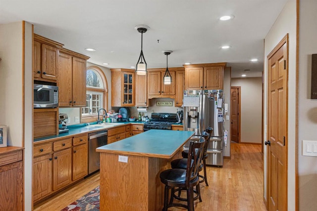 kitchen with a breakfast bar area, a sink, light wood-style floors, brown cabinets, and appliances with stainless steel finishes