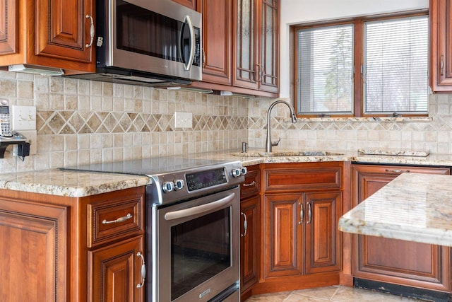 2151 Sunrise Dr, Appleton, WI 54914 - kitchen featuring light stone counters, a sink, decorative backsplash, brown cabinetry, and appliances with stainless steel finishes