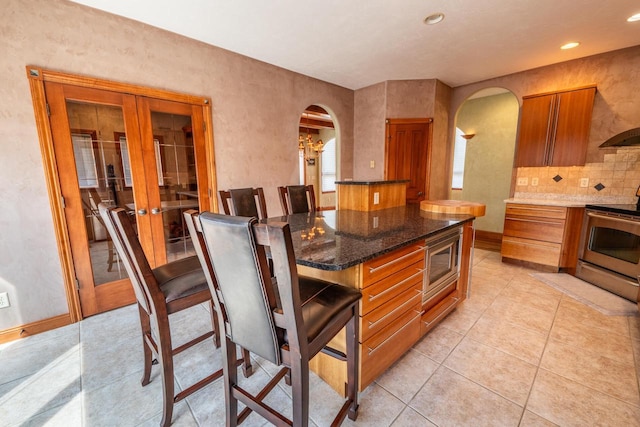 201 E Clearfield Ln, Appleton, WI 54913 - kitchen with arched walkways, stainless steel appliances, brown cabinets, light tile patterned flooring, and recessed lighting