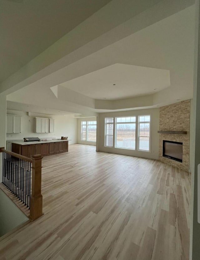 1618 White Deer Trl, Waukesha, WI 53189 - unfurnished living room featuring a stone fireplace, a tray ceiling, and light wood-style floors