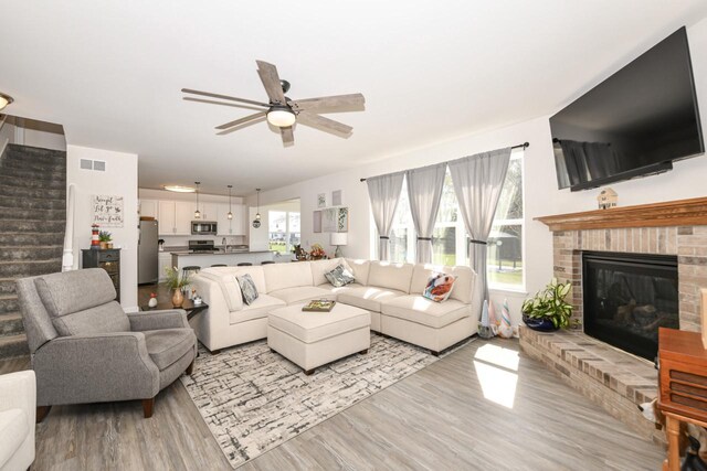 430 Ashley Dr, Williams Bay, WI 53191 - living area with light wood finished floors, visible vents, a ceiling fan, a brick fireplace, and stairs