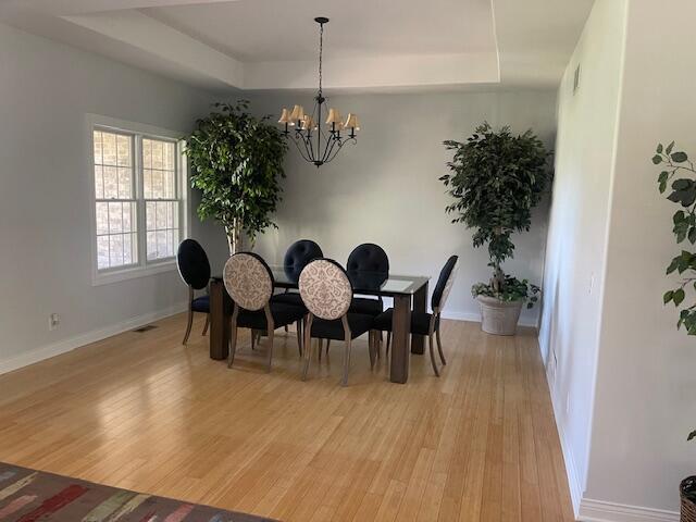 dining area with light wood-style flooring, baseboards, an inviting chandelier, and a raised ceiling
