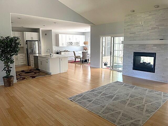 living room with lofted ceiling, a multi sided fireplace, and light wood-style flooring