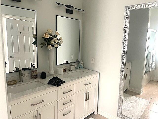 full bath featuring double vanity, tile patterned flooring, baseboards, and a sink