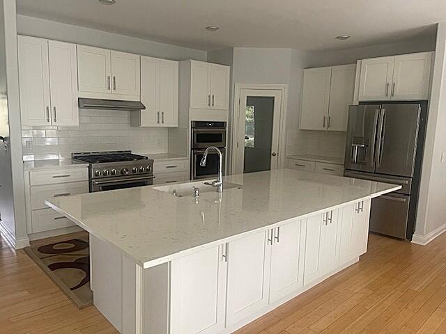 kitchen with stainless steel appliances, a sink, white cabinetry, light wood-style floors, and under cabinet range hood