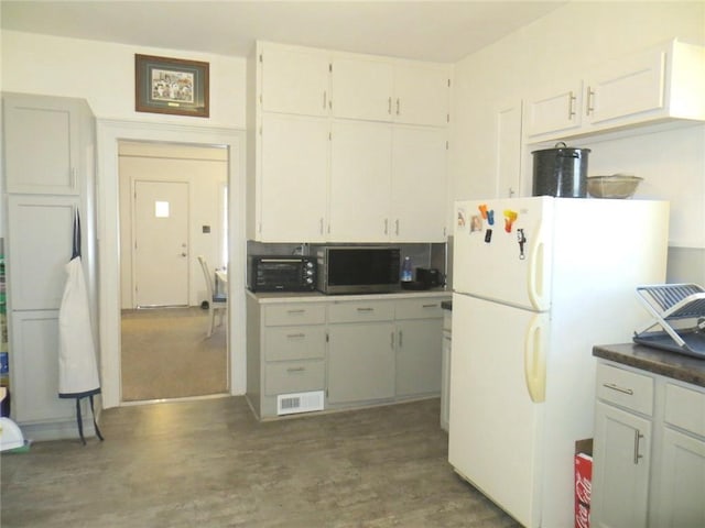 kitchen with dark wood-type flooring, freestanding refrigerator, visible vents, and white cabinetry