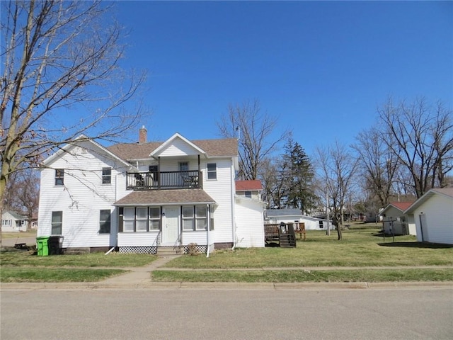 traditional home featuring a chimney, a front lawn, entry steps, a balcony, and roof with shingles