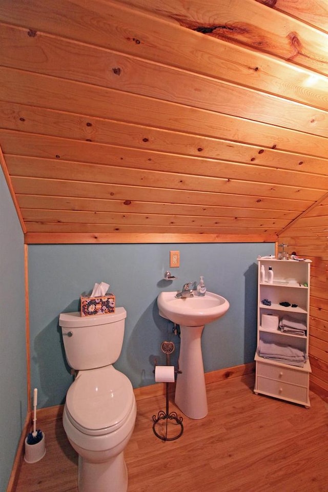 half bath with lofted ceiling, wood finished floors, toilet, and baseboards