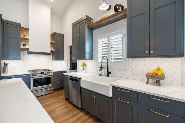 kitchen with stainless steel appliances, open shelves, a sink, light stone countertops, and tasteful backsplash