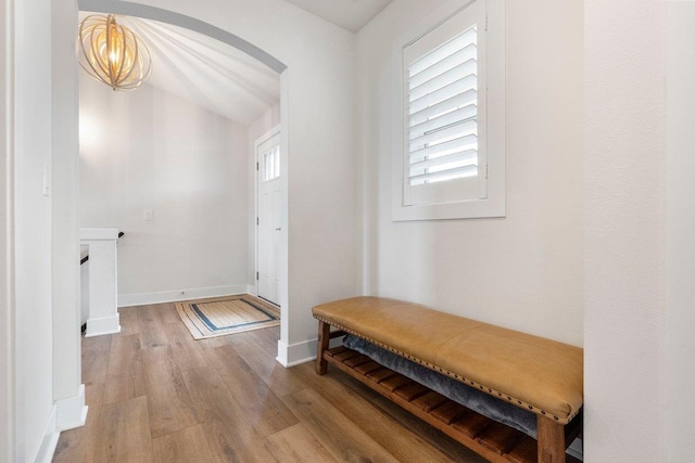 interior space featuring a chandelier, arched walkways, light wood-style flooring, baseboards, and lofted ceiling