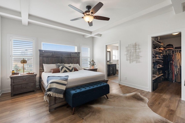 bedroom with beamed ceiling, ensuite bathroom, wood finished floors, and a walk in closet