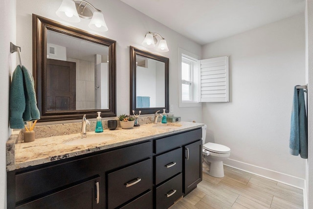 bathroom featuring double vanity, toilet, baseboards, and a sink