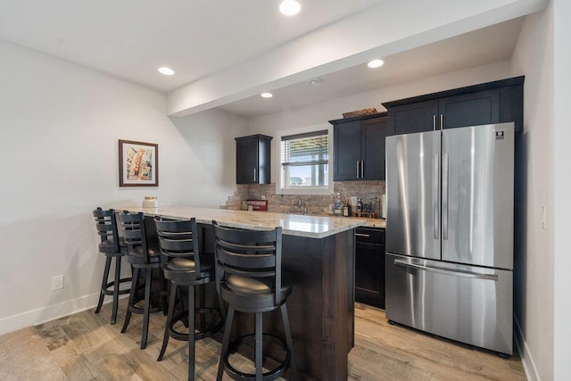 kitchen featuring a breakfast bar, freestanding refrigerator, light wood-style floors, and light stone counters