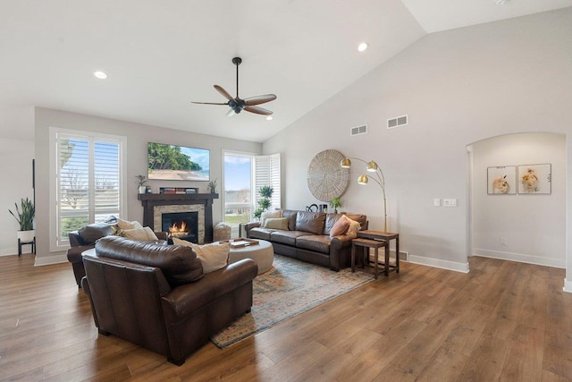 living area with a stone fireplace, visible vents, wood finished floors, arched walkways, and ceiling fan