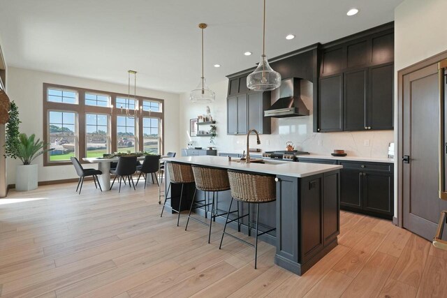 8437 Creek View Ln, Mount Pleasant, WI 53406 - kitchen featuring recessed lighting, an island with sink, light countertops, wall chimney range hood, and a kitchen bar