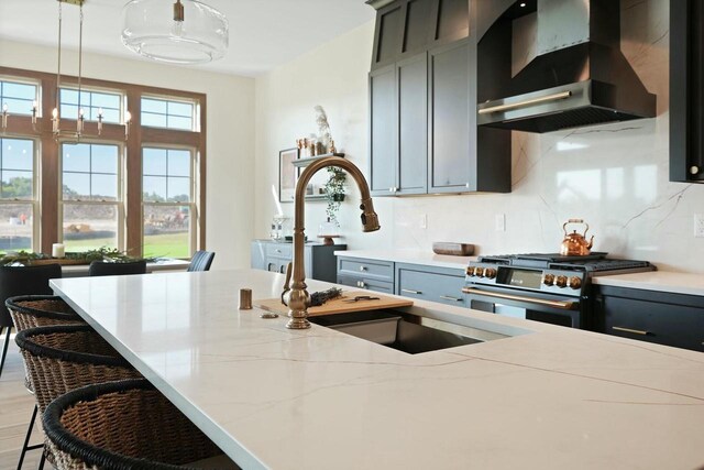 8437 Creek View Ln, Mount Pleasant, WI 53406 - kitchen featuring wall chimney exhaust hood, stainless steel range, backsplash, light stone counters, and decorative light fixtures