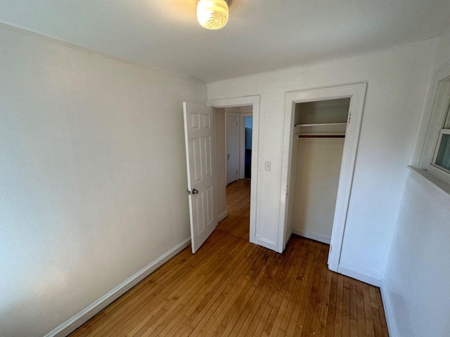 unfurnished bedroom featuring wood-type flooring, a closet, and baseboards