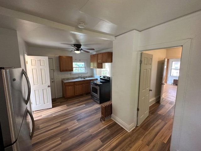 kitchen featuring stainless steel appliances, a sink, brown cabinets, ceiling fan, and dark wood-type flooring