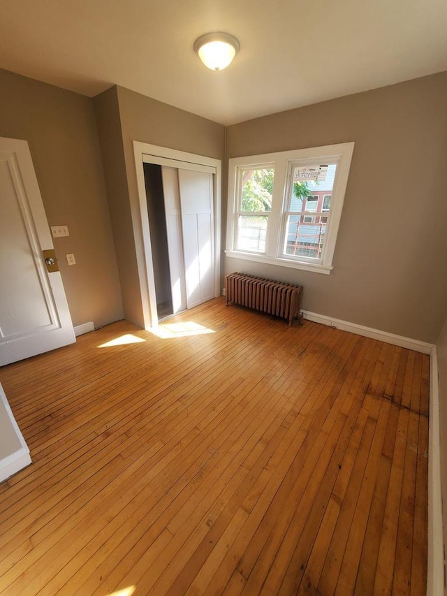 unfurnished bedroom featuring radiator heating unit, a closet, light wood finished floors, and baseboards