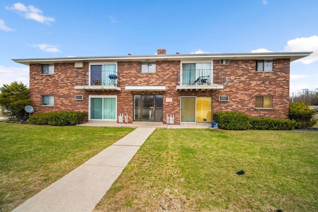 view of front of house featuring brick siding, a chimney, a front yard, and a balcony