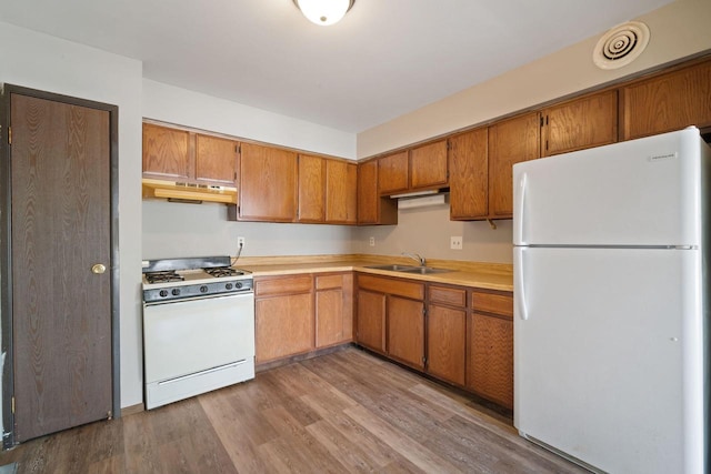 kitchen with light wood-style floors, white appliances, brown cabinetry, light countertops, and under cabinet range hood