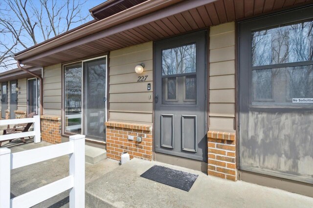 doorway to property featuring a porch and brick siding