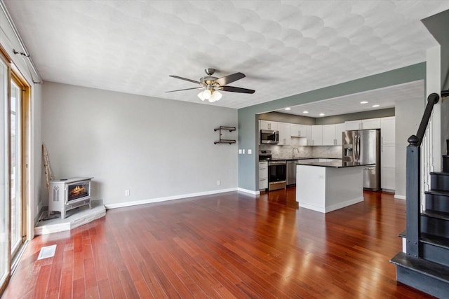 unfurnished living room with ceiling fan, a sink, a wood stove, baseboards, and dark wood-type flooring