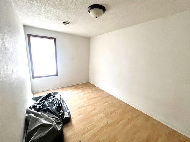 unfurnished room with baseboards, wood finished floors, visible vents, and a textured ceiling