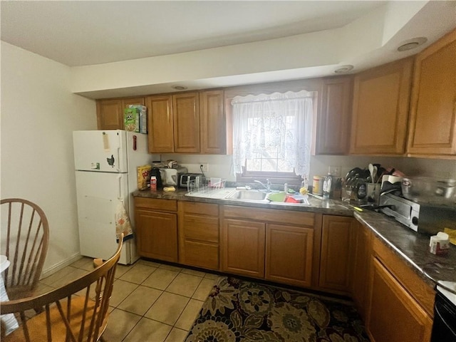 kitchen featuring a sink, dark countertops, freestanding refrigerator, brown cabinetry, and light tile patterned floors