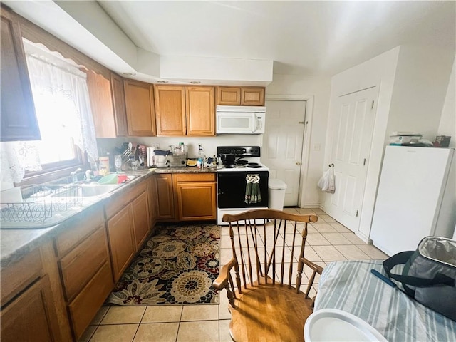 kitchen featuring light tile patterned flooring, electric stove, white microwave, and brown cabinets