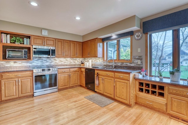 kitchen featuring light wood finished floors, open shelves, a sink, decorative backsplash, and appliances with stainless steel finishes