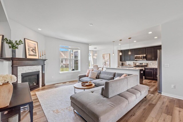 living room with recessed lighting, baseboards, light wood finished floors, and a stone fireplace