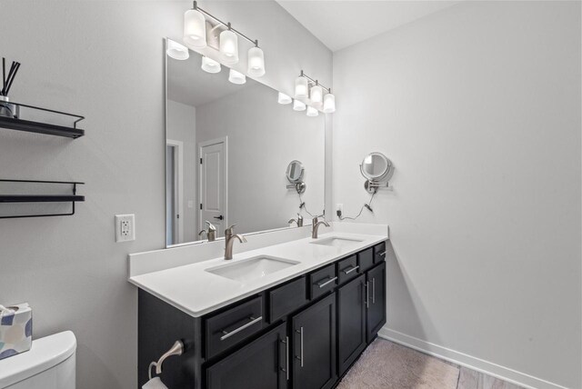 full bath with double vanity, toilet, baseboards, and a sink