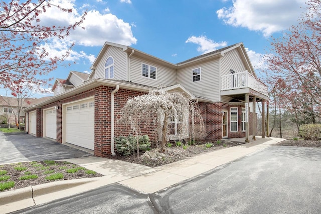 view of front of home featuring aphalt driveway, a balcony, and brick siding