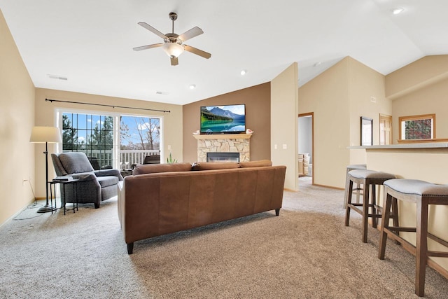living room with a ceiling fan, a stone fireplace, vaulted ceiling, baseboards, and light colored carpet