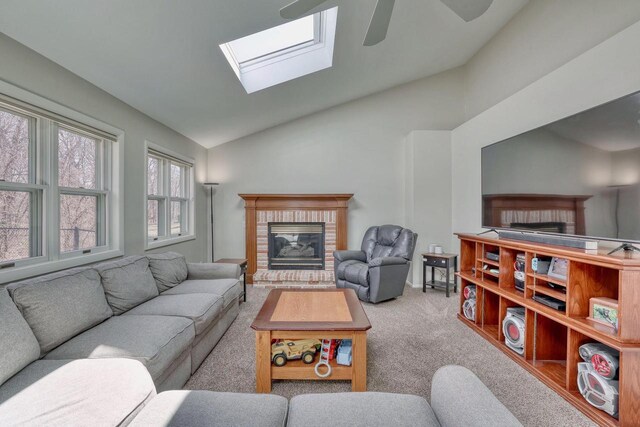 living area featuring ceiling fan, carpet floors, vaulted ceiling with skylight, and a brick fireplace