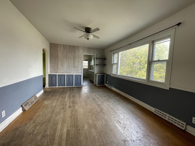 unfurnished living room featuring arched walkways, baseboards, visible vents, wood finished floors, and ceiling fan