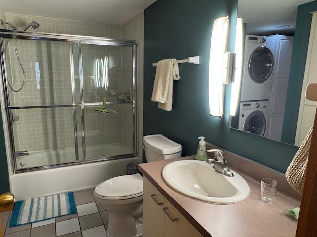 bathroom featuring tile patterned floors, shower / bath combination with glass door, toilet, stacked washer / drying machine, and vanity