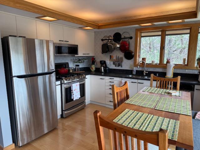 kitchen featuring light wood-style flooring, a sink, dark countertops, white cabinetry, and appliances with stainless steel finishes