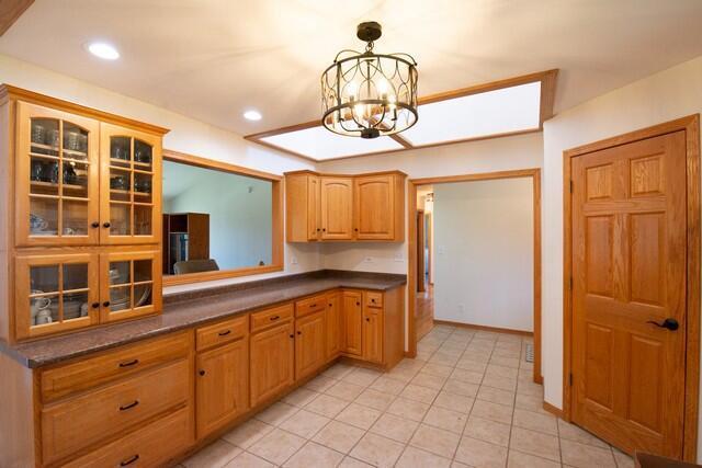 9506 296th Ave, Salem, WI 53168 - kitchen with light tile patterned floors, dark countertops, a chandelier, and glass insert cabinets