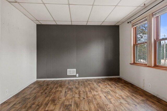 771 Seneca Rd, Wisconsin Rapids, WI 54495 - unfurnished room with a drop ceiling, wood walls, wood finished floors, visible vents, and baseboards