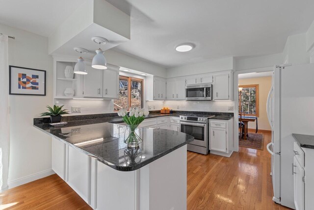 kitchen featuring stainless steel appliances, a peninsula, backsplash, light wood-style floors, and white cabinetry