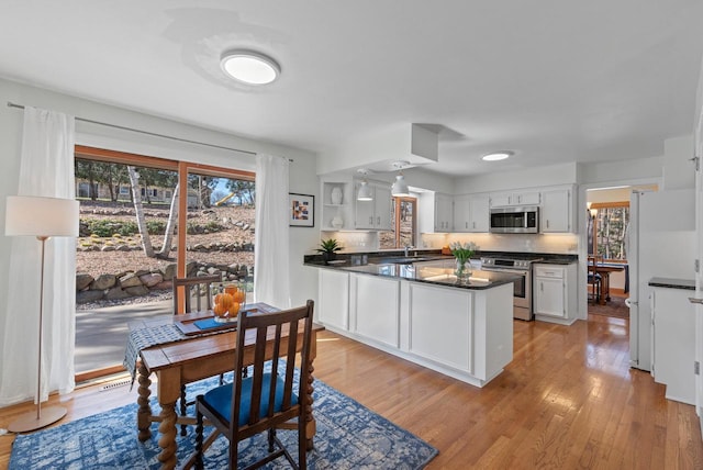 kitchen with open shelves, dark countertops, a peninsula, light wood-style flooring, and appliances with stainless steel finishes