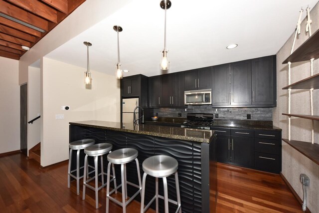 kitchen with range with gas stovetop, freestanding refrigerator, dark wood-type flooring, stainless steel microwave, and tasteful backsplash